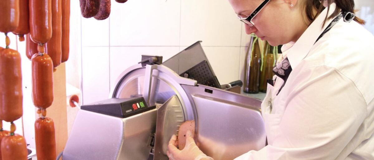 Fachverkäuferin steht vor einer Schneidemaschine und schneidet Wurst in Scheiben