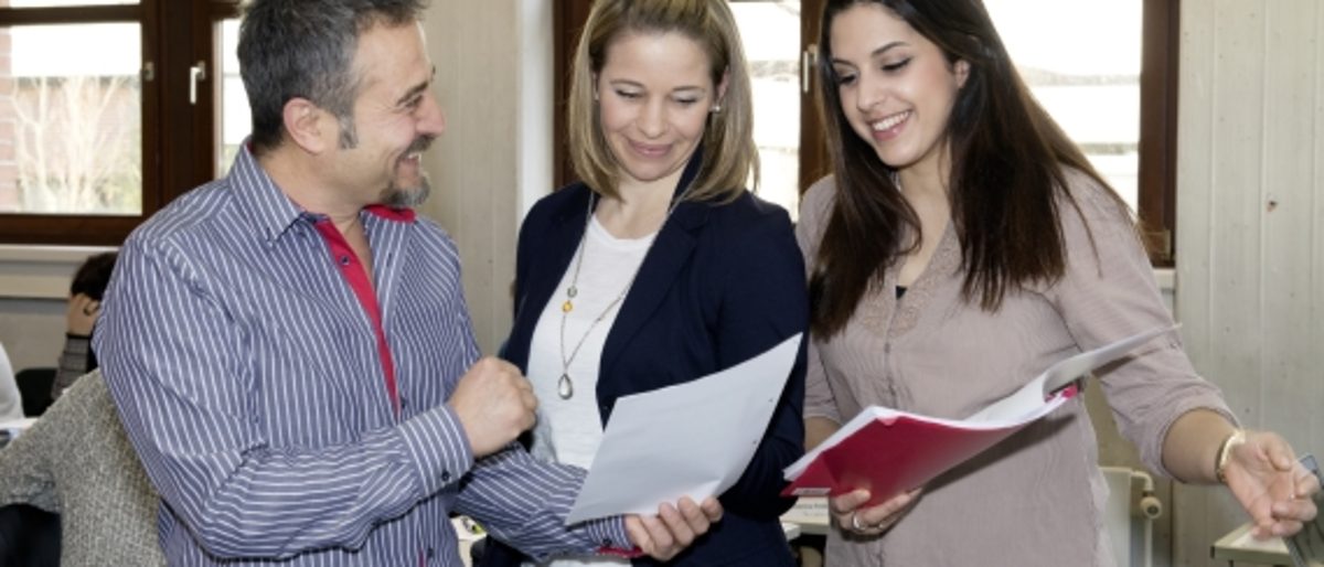 Drei Personen, ein Mann, eine blonde Frau, eine schwarzhaarige Frau, Migrationshintergrund, Gesprächssituation, Diskussion, Team, Teamarbeit, Büro, Schulungsraum, Schulung, Weiterbildung, Fragen, Antworten, Zeigen, freundlich, Lächeln